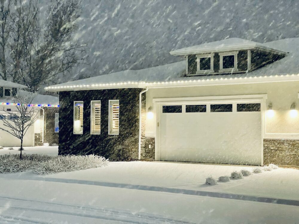 Suburban home with holiday lights in a snowstorm at night